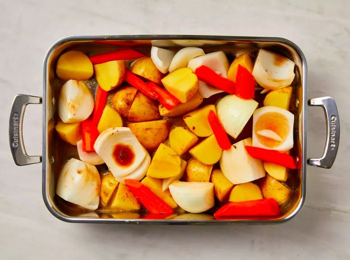 Roasting pan filled with potatoes, carrots, onions, and a rich brown liquid.