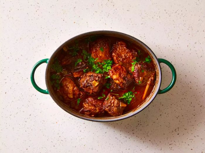 Braised beef short ribs in a pot, topped with fresh herbs.