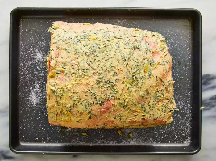 An overhead view of a roast on a baking sheet, topped with the butter mixture.