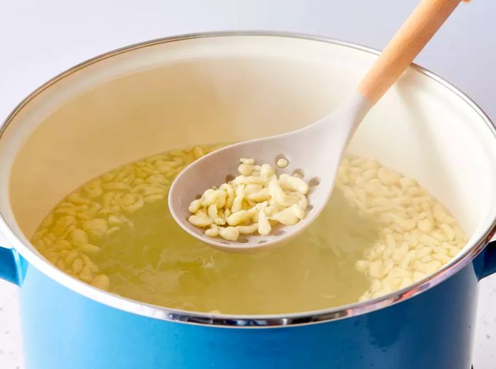 Spaetzle being lifted with a slotted spoon after it has floated to the top of the water.