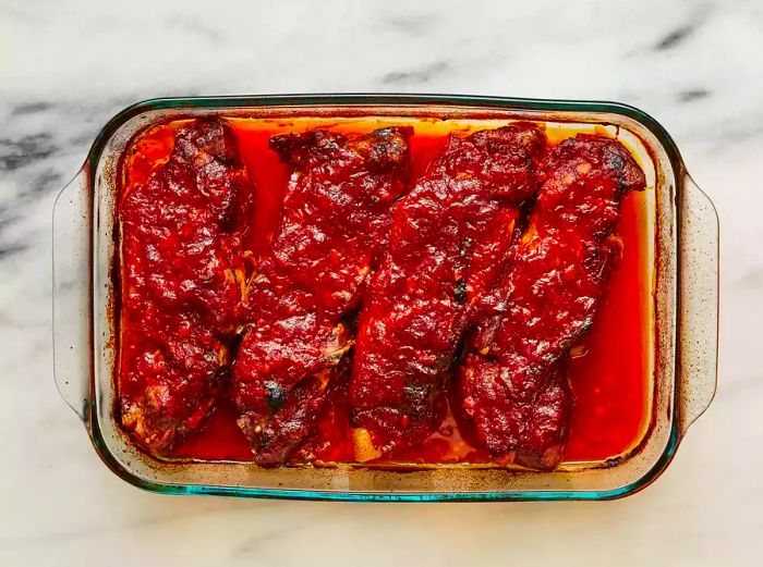 Oven-Roasted Ribs coated in barbecue sauce, resting in a baking dish