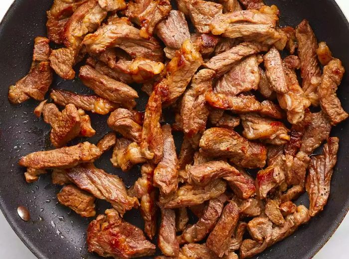 Aerial view of beef cooking in a skillet.