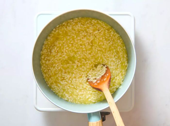 A pan of arborio rice and broth being stirred together with a wooden spoon