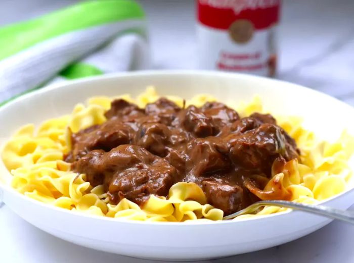 Creamy beef tips served over egg noodles in a white bowl.