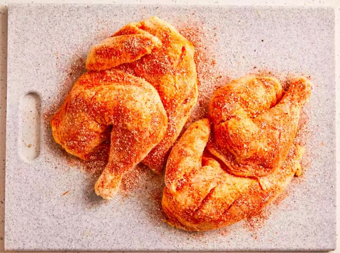 A top-down view of barbecue chicken seasoned with salt, pepper, paprika, onion powder, and cayenne pepper on a cutting board