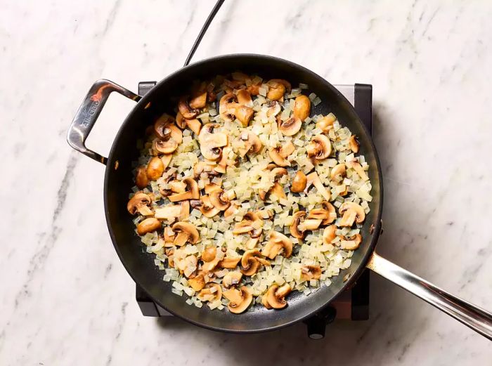 Mushrooms and onions sautéing in the skillet until tender.