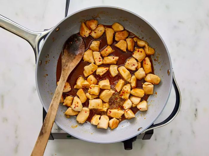 Aerial view of cubed chicken being stirred in a skillet with honey glaze