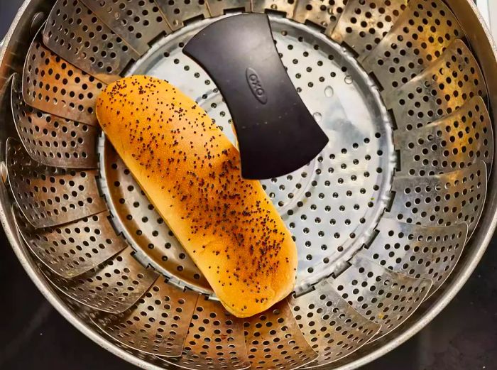 A bird's-eye view of a poppy seed hot dog steaming in a basket.