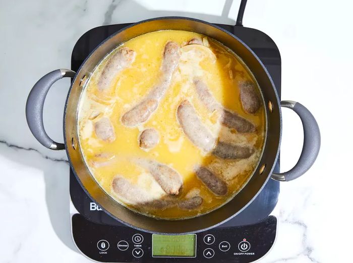 A top-down view of bratwursts simmering in a stockpot with beer, onions, butter, and black pepper