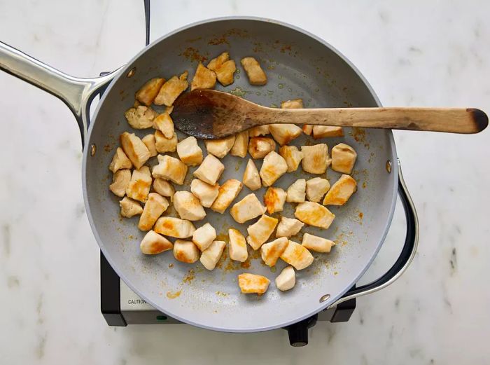 Aerial view of cubed chicken browning in a skillet