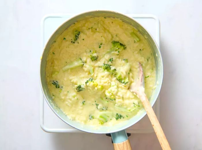 A pot of creamy broccoli risotto being stirred with a wooden spoon