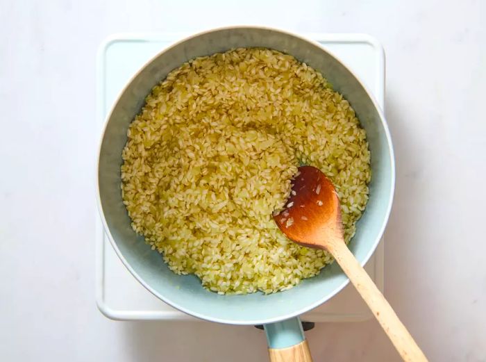 A pan with arborio rice being mixed with chopped onion, garlic, and oil