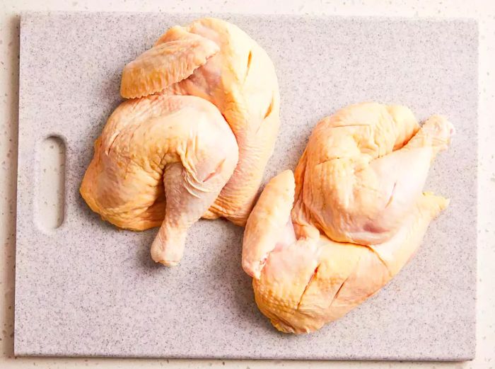 A top-down view of raw chicken thighs and wings with deep cuts on a cutting board