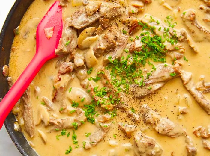 Aerial view of beef stroganoff being stirred and cooked in a skillet.