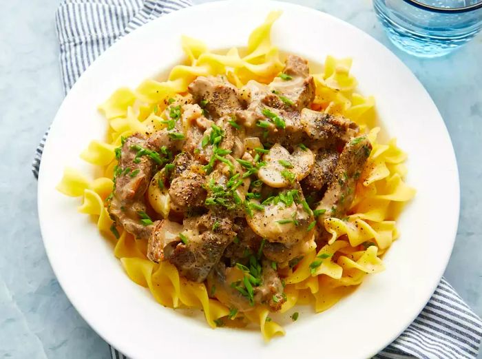 Close-up of a bowl of classic beef stroganoff served over pasta, topped with fresh herbs.