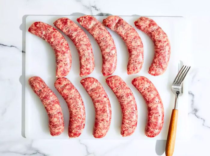 A top-down view of bratwursts on a cutting board, pierced with a fork