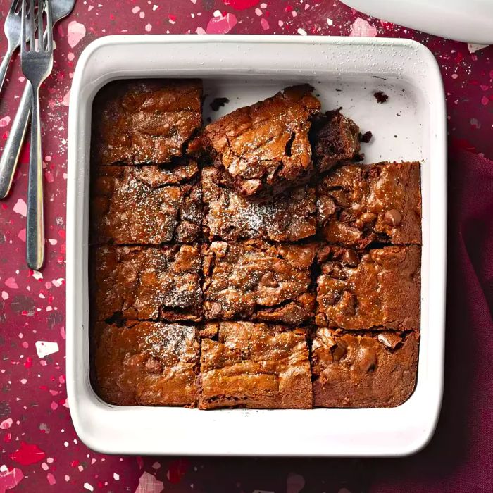 A square white baking dish filled with perfectly cut Brooke's Best Bombshell Brownies, neatly divided into 12 pieces with two removed.