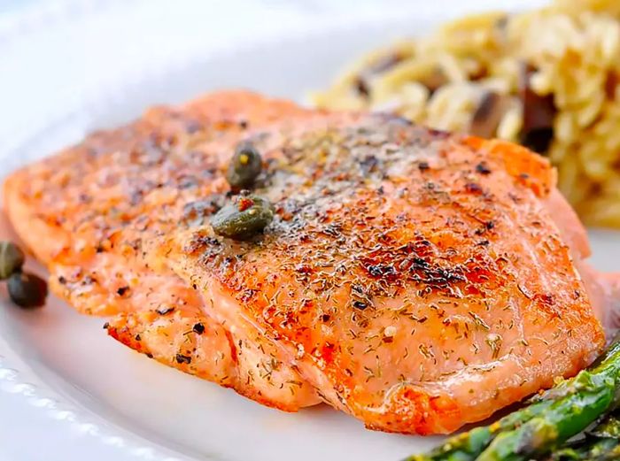 A view from eye level of a pan-seared salmon fillet served with asparagus and wild rice.