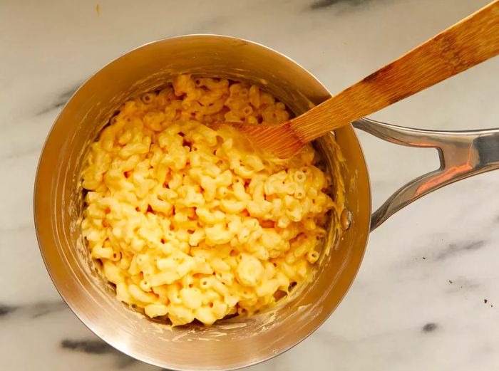 An overhead view of a pan with cheese sauce being mixed with macaroni.