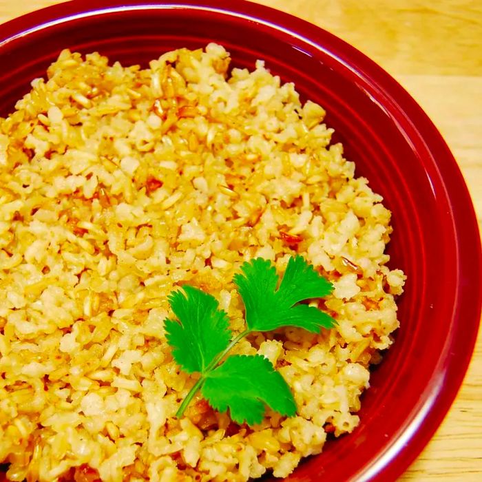 A red ceramic bowl filled with brown rice, topped with a sprig of fresh cilantro.