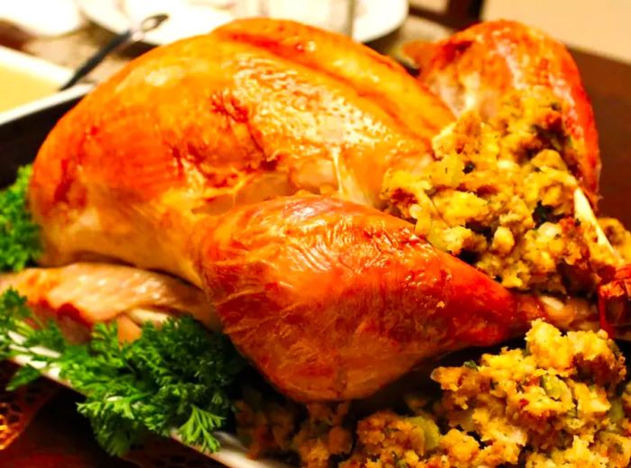 A close-up view of a roasted turkey that’s been citrus-brined, with stuffing and fresh herbs on a platter