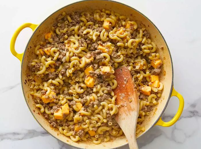 Chunks of cheese being added to the skillet with macaroni and ground beef