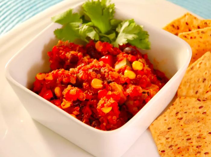 A close-up view of Quinoa and Black Bean Chili, topped with fresh herbs in a white bowl, served with crispy tortilla chips on the side