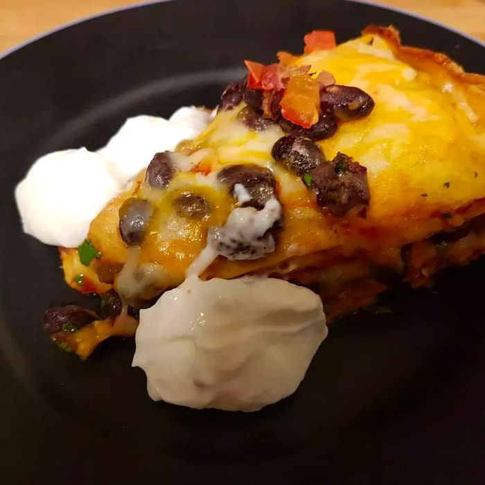 A slice of seven-layer tortilla pie topped with a dollop of sour cream