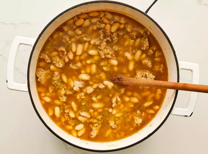 A large pot containing cannellini beans, chicken broth, and cooked ground turkey
