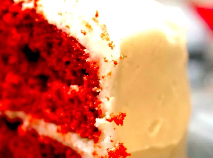 A close-up shot of a slice of Red Velvet Cake topped with creamy white icing