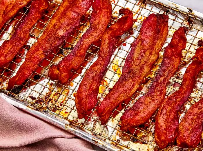 A foil-lined baking sheet topped with a wire rack and loaded with crispy, thick-cut bacon