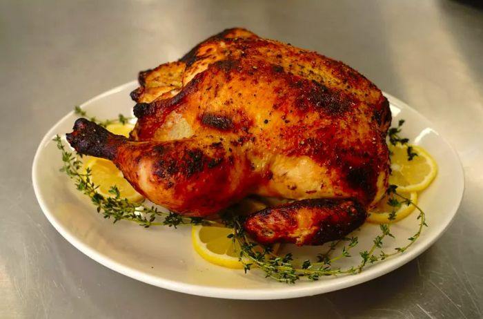 A whole roasted chicken served on a plate, garnished with fresh thyme and lemon slices.