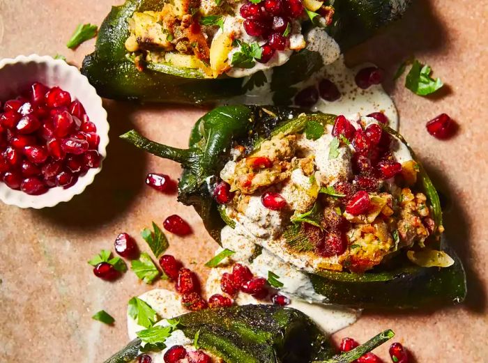 A close-up of three chiles en nogada on a board, accompanied by a side of pomegranate seeds