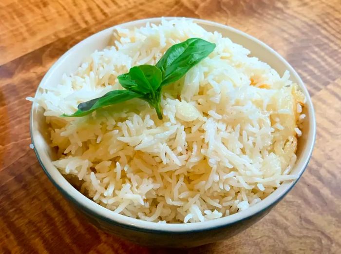 Close-up of Coconut Jasmine Rice served in a white bowl, topped with fresh basil leaves.