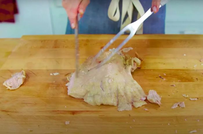 Carving a chicken thigh on a cutting board.