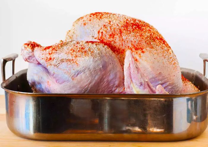 Uncooked turkey coated with a dry rub inside a roasting pan