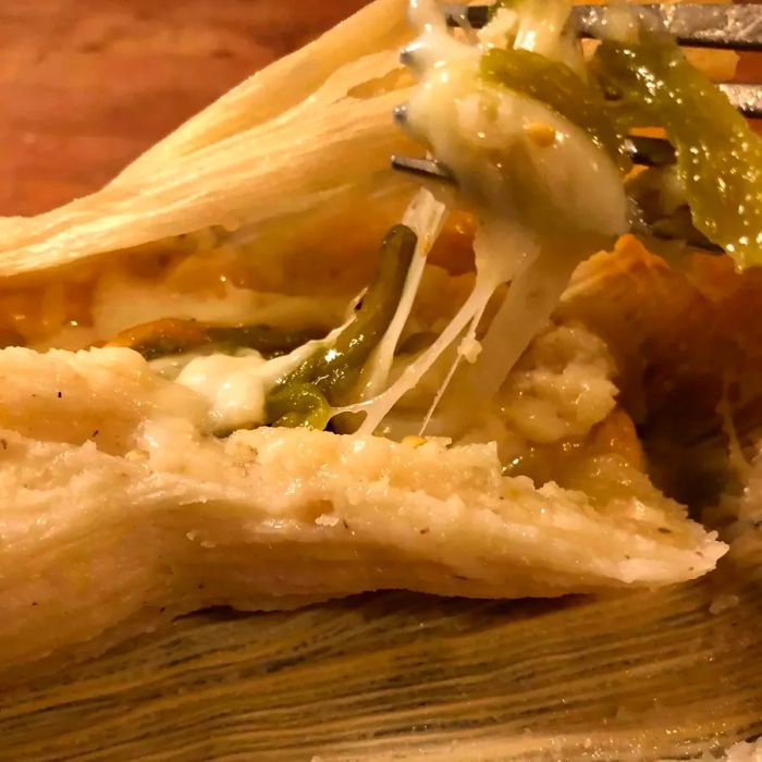 A fork cutting into a steaming poblano and cheese tamale