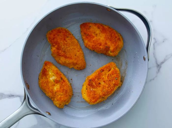 Chicken cutlets sizzling in a skillet.