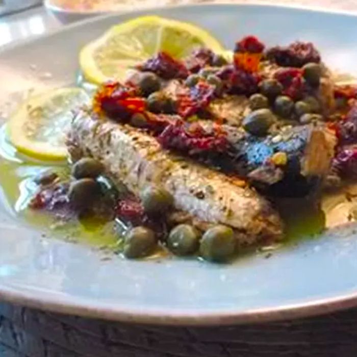 A plate of sardines topped with capers, sun-dried tomato strips, and lemon slices