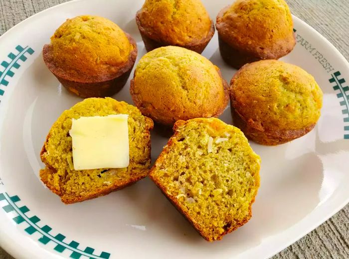 A plate of banana coconut muffins, one sliced open with a pat of butter on top