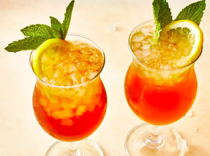 Two tall glasses of Long Island Iced Tea, each adorned with mint and fresh lemon slices.