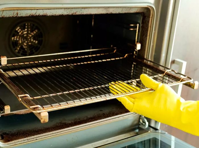 Close-up image of a man wearing yellow protective gloves cleaning an oven.