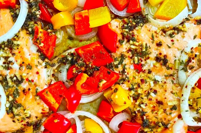 An overhead shot of perfectly roasted salmon and colorful bell peppers on a foil-lined baking sheet.