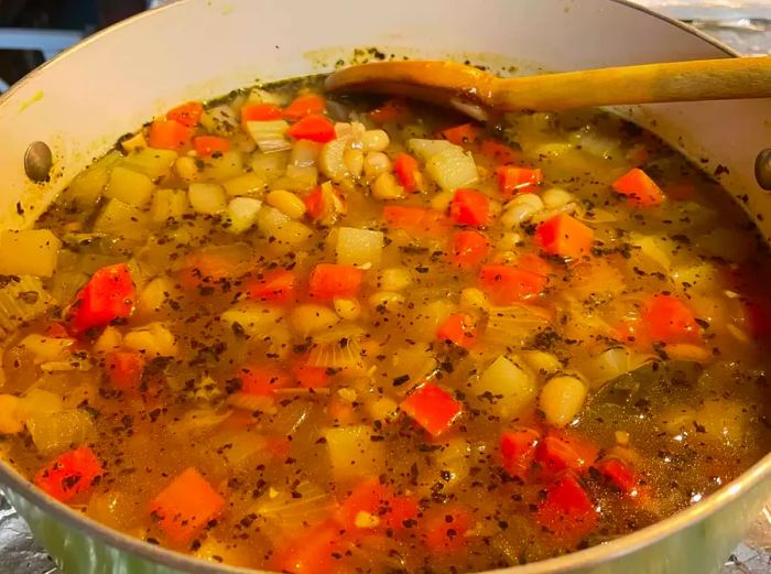 A close-up shot of Great Northern Bean Soup simmering in a pot with a wooden spoon resting inside