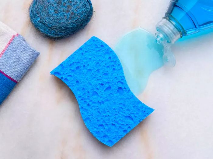 Overhead shot of blue dish soap, a sponge, and a brillo pad resting on a counter