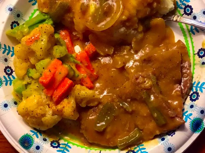 A plate featuring mashed potatoes, savory gravy, Grandma's Slow Cooker Swiss Steak, and a side of mixed vegetables.