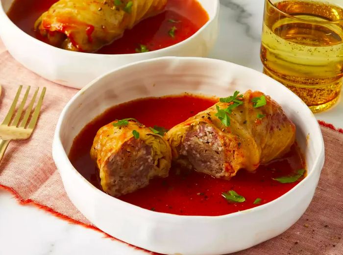 A close-up shot of Grandma’s Hungarian stuffed cabbage, sliced in half and served in a bowl with rich tomato sauce and garnished with fresh herbs.