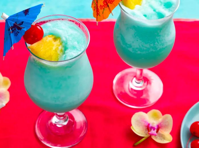 A high-angle shot of two Blue Hawaiian cocktails garnished with pineapple and cherries.