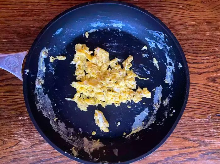 A mound of scrambled eggs sits in the middle of a nonstick pan, with stubborn egg residue clinging to the surface.