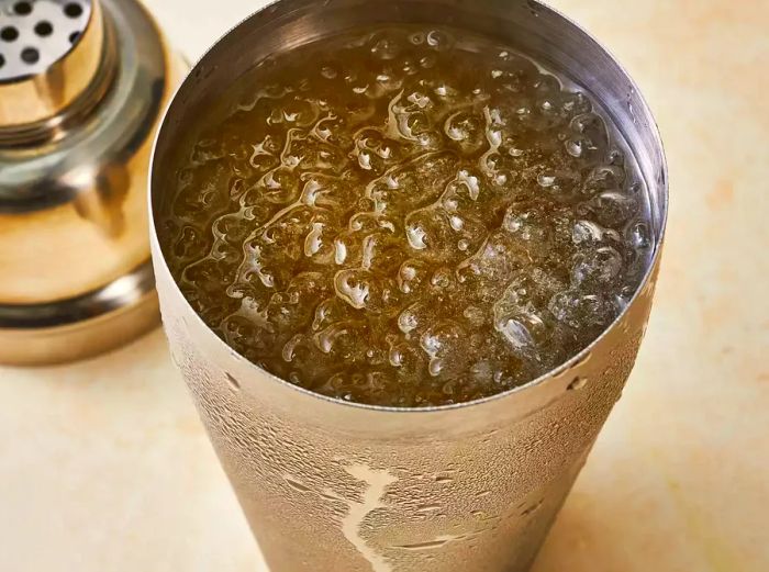 A cocktail shaker filled with vodka, rum, gin, tequila, triple sec, and sour mix, all resting on ice.